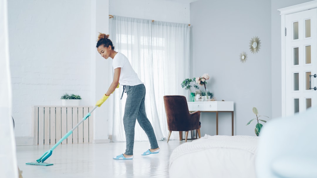 brand-02 Pretty African American girl is mopping the floor at home with a flat plastic mop, wearing gloves and comfortable home clothes. Modern interiors, cleanliness, and young people concept.